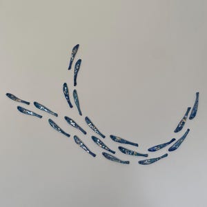 May include: A decorative wall art piece depicting a shoal of small, blue fish with iridescent details. The fish are arranged in a curved formation against a white wall, creating a sense of movement. The artwork is reminiscent of marine life.