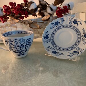 May include: A white teacup and saucer with a blue floral pattern. The cup and saucer have a scalloped edge.