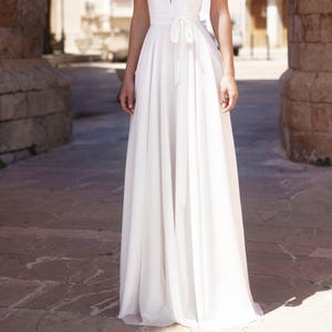 May include: A white maxi dress with a V-neckline and a sash tied at the waist.