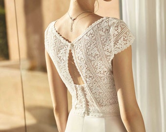 May include: A white lace wedding dress with a low back and a fitted bodice. The dress has a delicate floral pattern and a simple, elegant design.