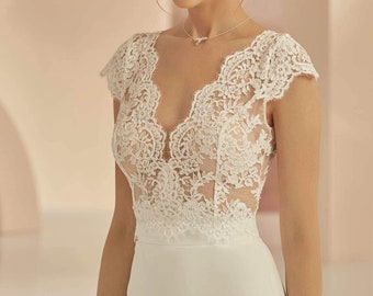 May include: A white wedding dress with a lace bodice and a fitted skirt. The bodice has a deep V-neckline and short cap sleeves. The lace is delicate and intricate.