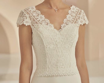 May include: A white lace wedding dress with a V-neckline and short sleeves. The bodice is made of delicate lace and the skirt is a simple, flowing silhouette.