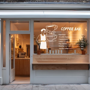 Pu&ograve; includere: Vista esterna di un bar con tenda da sole e finiture bianche. La vetrina mostra una grafica di tazza di caff&egrave; e un menu. Un personaggio grafico tiene un vassoio con tazze di caff&egrave;. Il menu elenca espresso, cappuccino e altre bevande.