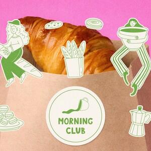 Pu&ograve; includere: Un sacchetto di carta marrone pieno di un croissant. Illustrazioni verdi e bianche di articoli per la colazione e persone sono poste attorno alla borsa. Un adesivo rotondo con le parole "MORNING CLUB" &egrave; sulla borsa. Lo sfondo &egrave; rosa.