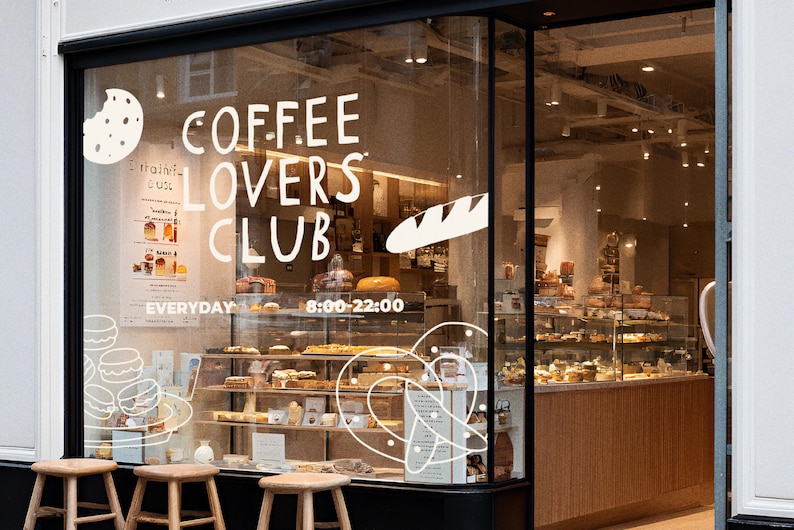 Pu&ograve; includere: Vetrina di un bar con la scritta "COFFEE LOVERS CLUB" e una selezione di pasticceria. L'orario di apertura &egrave; indicato dalle 8:00 alle 22:00. Sgabelli in legno sono posizionati davanti alla vetrina, offrendo uno sguardo all'interno.