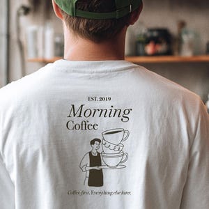 Pu&ograve; includere: T-shirt bianco con una grafica sul retro che dice "Morning Coffee" con una pila di tazze da caff&egrave; e una persona che tiene un vassoio. Il testo "Coffee first, Everything else later" &egrave; stampato anche sulla maglietta. La maglietta ha anche "EST. 2019" stampato.