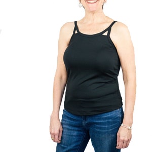 May include: A woman wearing a black tank top and blue jeans. She is smiling and looking at the camera.