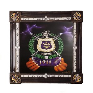May include: A framed domino set. The central graphic features a shield, swords, and the Greek letters ΩΨΦ, with the year 1911. The dark brown frame has dominoes along the edges and decorative corner pieces.