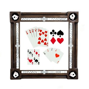 May include: A wooden domino table with a white playing surface and a brown wooden frame. The table has a built-in scoring system and is designed for playing dominoes. There are also playing cards on the table, including a set of playing cards with a red heart suit and a set of playing cards with a black spade suit.