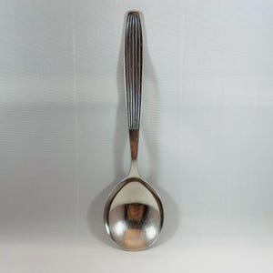 Könnte beinhalten: Ein silberner Suppenlöffel mit einem langen, schlanken Stiel mit einem gerillten Design.