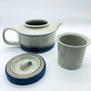 May include: A white ceramic teapot with a blue and brown striped design, a matching lid, and a separate white ceramic strainer.