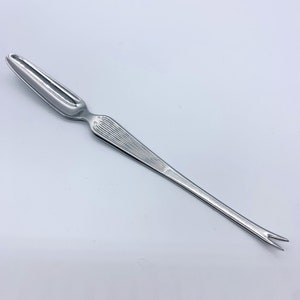 Könnte beinhalten: Eine silberne Austern-Gabel mit einem langen, dünnen Stiel und einer kleinen, abgerundeten Kelle oben. Der Stiel hat ein dekoratives, geripptes Muster.