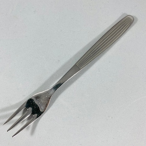 Könnte beinhalten: Eine Edelstahlgabel mit drei Zinken. Der Griff hat eine Reihe paralleler, erhabener Linien für einen besseren Halt. Die Gabel ist zum Servieren oder Essen kleiner Portionen bestimmt.