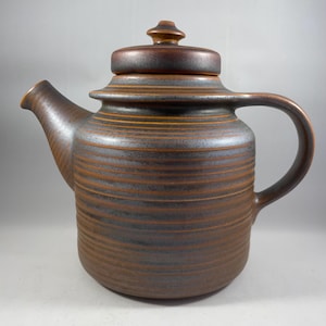 Peut inclure: Une théière en céramique brune avec un couvercle et un motif rayé. La théière a un bec verseur et une anse.