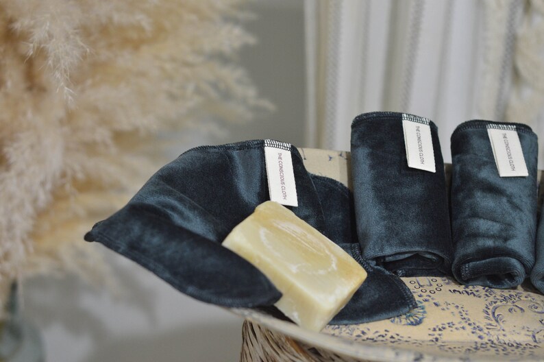 Peut inclure: Quatre linges en velours bleu fonc&eacute; pli&eacute;s et empil&eacute;s dans un bol &agrave; motifs blancs et bleus. Une barre de savon repose sur les linges. Les linges portent une &eacute;tiquette blanche avec le texte "The Conscious Cloth" imprim&eacute; dessus.