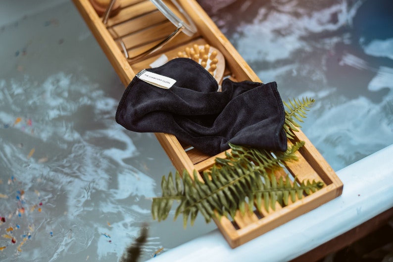 Peut inclure: Un gant de toilette noir avec le texte "The Conscious Co." sur un plateau en bois avec une foug&egrave;re verte. Le plateau est dans une baignoire avec de l'eau.
