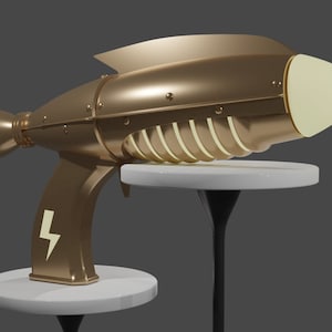 May include: A gold-colored toy ray gun with a white tip and a lightning bolt symbol on the handle. The gun is on a white pedestal.