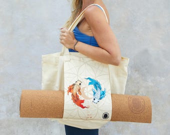 Pode incluir: Bolsa tote creme com um design de peixes koi, segurando um tapete de ioga enrolado. O tapete de ioga é castanho. A bolsa tem um padrão geométrico e um logotipo circular. Os peixes koi são vermelhos e azuis.