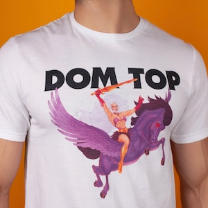Pode incluir: Camiseta branca com uma estampa preta das palavras "DOM TOP" e um gr&aacute;fico de uma mulher montando um cavalo alado.