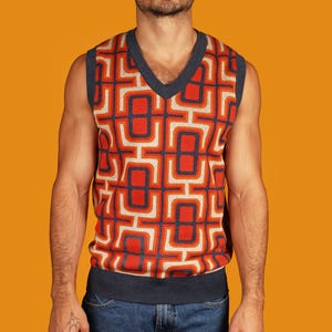 May include: A sleeveless sweater vest with a geometric pattern in shades of orange, red, and blue. The vest has a V-neck and a navy blue trim.