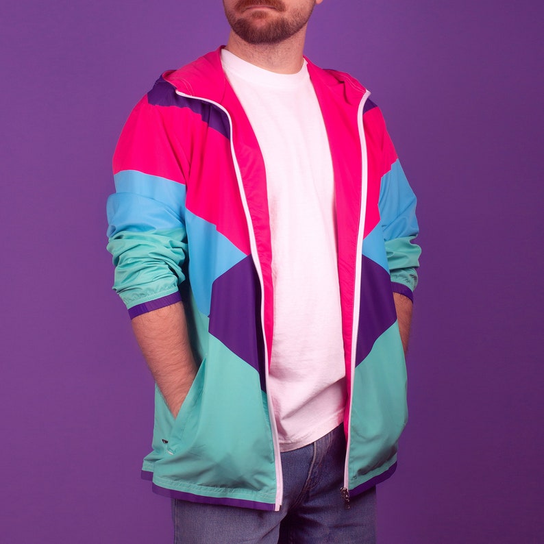 Pu&ograve; includere: Giacca multicolore nei toni del rosa, turchese, viola e blu con cerniera e cappuccio bianchi. La giacca ha uno stile retr&ograve; anni '80 o '90. Il modello indossa una maglietta bianca e jeans blu. La giacca ha due tasche anteriori.