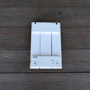 May include: White wooden wall shelf with three shelves and the word "Wooden" printed on the bottom shelf.