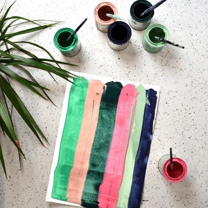 Puede incluir: Una hoja de papel blanca con cinco franjas verticales de pintura en tonos de verde, rosa, melocot&oacute;n y azul. La pintura se aplica en una capa gruesa y texturizada. Hay varios botes de pintura peque&ntilde;os en el fondo, algunos con pinceles.