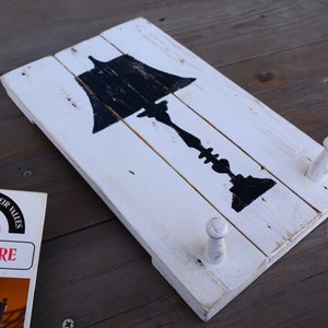 May include: White wooden wall decor with a black silhouette of a lamp and two white wooden hooks.