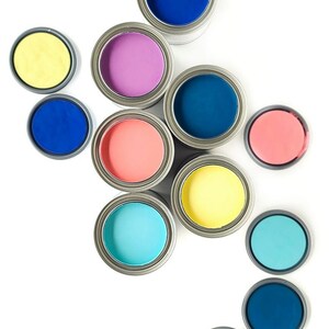 May include: An assortment of paint cans in various colours, including blue, purple, yellow, pink, orange, and turquoise. The cans are arranged in a semi-circle on a white background.