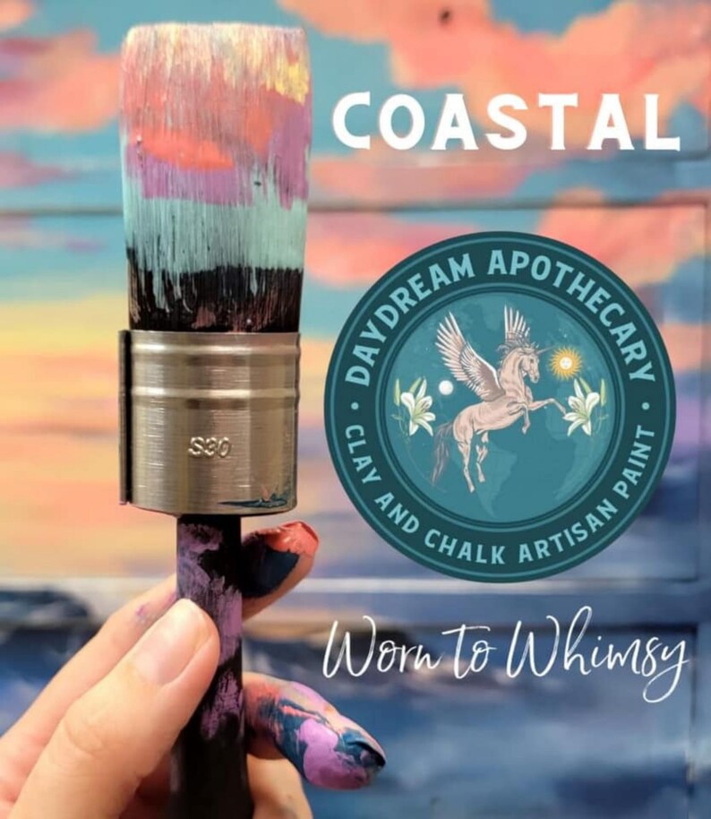 May include: A hand holds a paintbrush with a colourful, layered paint design. The brush is labelled "S20". The background features a sunset sky with the words "COASTAL" and "Worn to Whimsy". A circular logo reads "Daydream Apothecary Clay and Chalk Artisan Paint" with a winged unicorn and floral design.