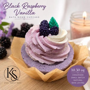 May include: A Black Raspberry Vanilla bath bomb cupcake with a purple base, swirled light purple and white frosting, topped with two dark purple blackberries and a green leaf. The product label states 10.30 oz, handmade, small batch, natural, skin loving.