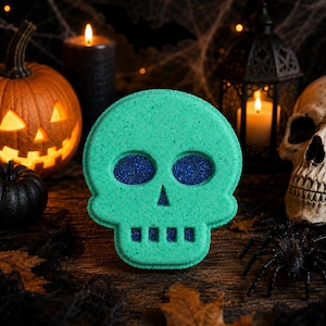 May include: A skull-shaped bath bomb in a vibrant matte green finish. The design features deep-set eye sockets, a triangular nasal cavity, and rectangular teeth cutouts, all filled with a contrasting dark blue, fine-grained glitter texture.