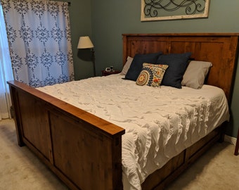 May include: A wooden bed frame with a white ruffled bedspread and pillows. The headboard is made of wood planks and has a rustic look.