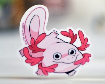 May include: A pink axolotl with red gills, smiling, on a white sticker with the text "©2019 ANDY KLUTHE".