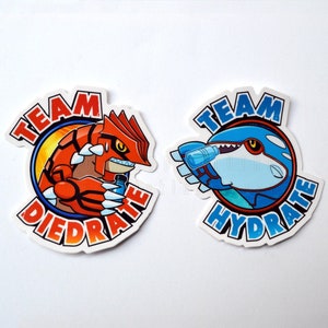 May include: Two round stickers with cartoon characters. The left sticker is red and orange with a red monster holding a bottle of water and the text "Team Dehydrate". The right sticker is blue and green with a blue shark holding a bottle of water and the text "Team Hydrate".