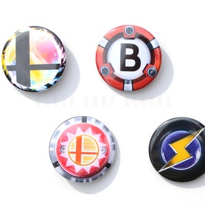 May include: Four round buttons with different designs. The first button has a black and white Smash Bros. logo with a colorful background. The second button has a red background with a white letter B in the center. The third button has a red background with a yellow sun and a black and white Smash Bros. logo. The fourth button has a black background with a purple circle and a yellow lightning bolt.