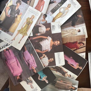 Może przedstawiać: Kolekcja różnych kopert z wykrojami krawieckimi Vogue, zawierająca ilustracje różnorodnych ubrań, w tym sukienek, garniturów i bluzek. Każda papierowa koperta prezentuje projekt modowy, nazwy marek takich jak Guy Laroche i Donna Karan oraz szczegóły techniczne konstrukcji odzieży.