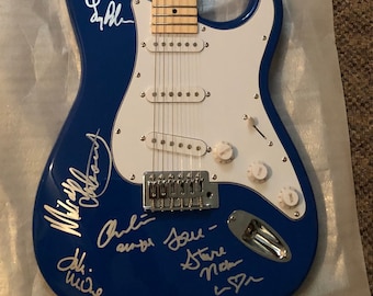May include: A blue electric guitar with white accents and multiple signatures on the body. The signatures include "Mike McCready", "Chris Cornell", "Jeff Ament", "Stone Gossard", and "Matt Cameron".