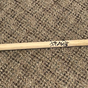 Puede incluir: Una baqueta de madera con una punta blanca, firmada "Frank" en tinta negra.