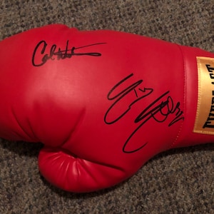 May include: Red boxing glove with black signatures of "Calzaghe" and "Joe Calzaghe" on the glove. The glove has a gold "EVERLAST" logo on the side.