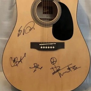 May include: A natural wood acoustic guitar with multiple signatures on the body, including "Chris Cornell", "Eddie Vedder", "Stone Gossard", and "Jeff Ament".