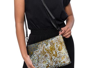 May include: A rectangular crossbody bag featuring a marbled pattern in shades of gold, white, and dark gray. The bag has a black adjustable strap attached to the sides with metal hardware, providing a functional way to carry personal items.