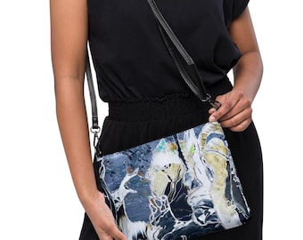 May include: A rectangular crossbody bag featuring an abstract marble-like pattern in shades of navy blue, white, and gold. The bag includes a thin black adjustable shoulder strap with metal hardware, worn across the torso over a black outfit.