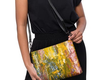 May include: A rectangular crossbody bag featuring an abstract paint drip pattern in vibrant shades of yellow, green, pink, and white. The bag includes a thin, adjustable black shoulder strap attached with metal hardware, providing a functional accessory.