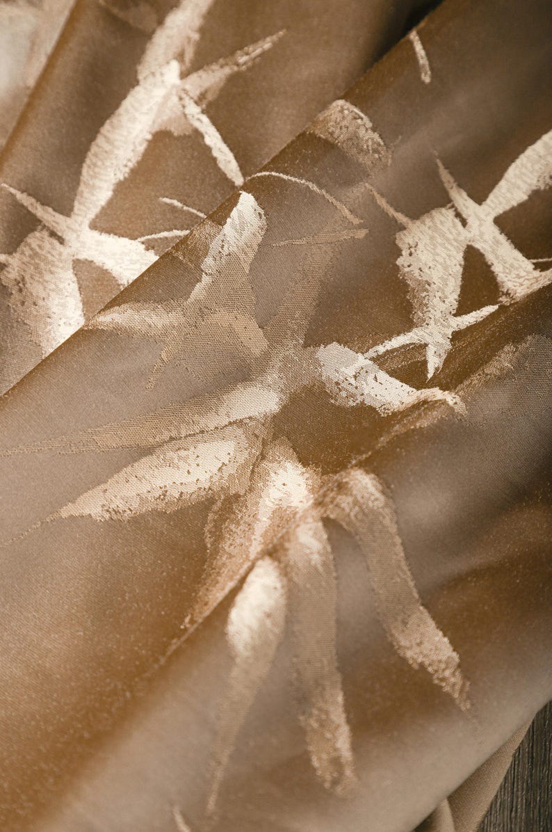 Puede incluir: Primer plano de una tela doblada con una superficie texturizada. La tela es de color marr&oacute;n c&aacute;lido con un patr&oacute;n de dise&ntilde;os blancos similares a pinceladas. La luz se refleja en la tela, creando reflejos y sombras.