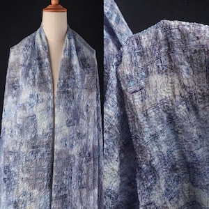 May include: A draped fabric with a textured, abstract pattern in shades of blue, gray, and white. The fabric is displayed on a mannequin, showcasing its drape and design. The close-up reveals the intricate details of the pattern.