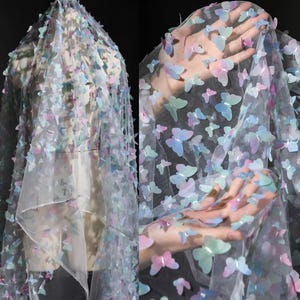 May include: Delicate sheer fabric decorated with multiple pastel butterfly appliqués. The butterflies feature shades of blue, pink, and green, creating a soft, dreamy appearance. The fabric is draped, highlighting its flowing texture and design.