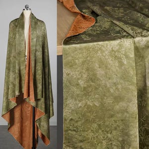 Könnte beinhalten: Ein wendbarer Schal in Grün- und Rosttönen. Der Schal wird auf einer Schaufensterpuppe präsentiert, um die Textur und das Design des Stoffes hervorzuheben. Der Stoff hat ein zartes Blumenmuster.