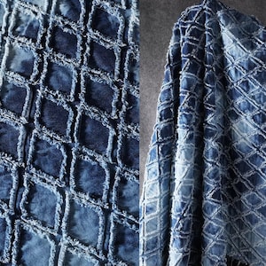 Könnte beinhalten: Nahaufnahme eines Denim-Stoffs mit einem Rautenmuster. Der Stoff ist ein tiefes Indigoblau mit helleren blauen Akzenten, wodurch ein strukturierter, verwitterter Look entsteht. Die Rauten sind mit ausgefransten Kanten umrandet.