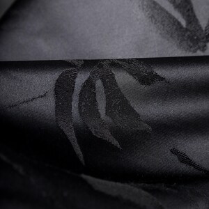 Puede incluir: Primer plano de tela negra con un patr&oacute;n sutil y repetitivo. La tela tiene una textura suave y satinada, con un ligero brillo. El patr&oacute;n parece ser un dise&ntilde;o estilizado de hoja o pluma.